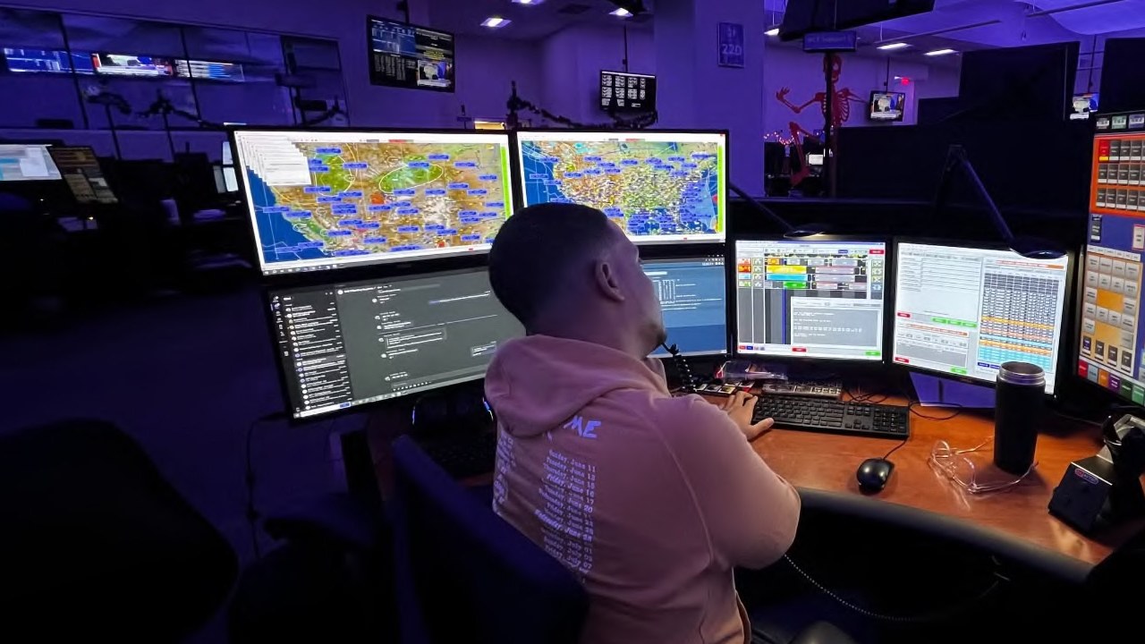 A Superintendent of Dispatch working across multiple monitors in a darkly-lit operations room.